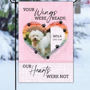 May include: A pink garden flag with a heart design, a white dog, and the name "Bella" with dates. The flag reads "Your Wings Were Ready; Our Hearts Were Not."