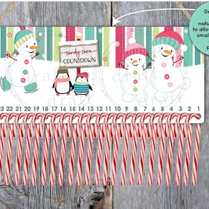 May include: A white and green candy cane countdown advent calendar with a snowman and penguin theme. The calendar has 24 candy cane holders and a sign that says "candy cane countdown".