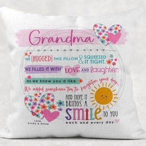 Op de afbeelding: Een wit kussen met een roze en groen bloemenontwerp. Het kussen heeft de tekst "Grandma" in roze letters en de tekst "WE HUGGED THIS PILLOW & SQUEEZED IT TIGHT. WE FILLED IT WITH LOVE AND laughter, as we knew you'd like. We added sunshine too, to brighten your day. AND HOPE IT BRINGS A smile TO YOU each and every day." in kleurrijke letters.