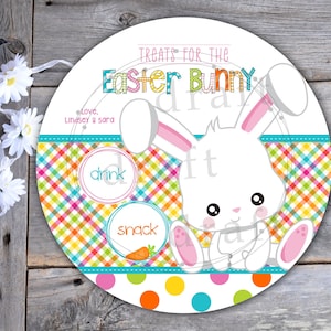 May include: A white Easter bunny with pink ears and a carrot sits on a colorful checkered background. The text "Treats for the Easter Bunny" is at the top of the circle. The text "Love, Lindsey & Sara" is below the bunny. The words "drink" and "snack" are in circles on the checkered background.