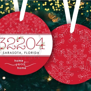 May include: Red and white Christmas bauble with a snowflake pattern. The bauble has a white band with the text "32204 Sarasota, Florida" and the phrase "home sweet home".