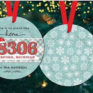 May include: Two round Christmas ornaments. One ornament is blue with a white snowflake pattern. The other ornament is blue with a red and white plaid pattern and the text "There is no place like home 48306 WATERFORD, MICHIGAN for the holidays."