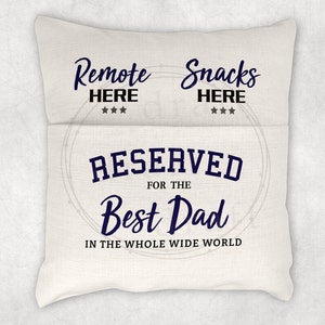 May include: A white pillow with the text "Remote Here" and "Snacks Here" on the top and the text "Reserved for the Best Dad in the Whole Wide World" in the center.