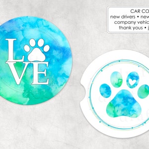 May include: Two round car coasters with a watercolor design. One coaster features a white paw print with the word "LOVE" in white letters. The other coaster features a blue and green watercolor paw print.