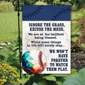 May include: A blue and white garden flag with a watercolor baseball design. The text on the flag reads: "IGNORE THE GRASS, EXCUSE THE MESS. We are at the ballfield being blessed. While some things in life will surely stay... WE WON'T HAVE FOREVER TO WATCH THEM PLAY."