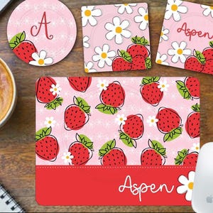 Könnte beinhalten: Ein rosa und rotes Mauspad mit einem Erdbeer- und Gänseblümchenmuster. Das Mauspad hat einen roten Rand und der Name "Aspen" ist unten aufgedruckt.