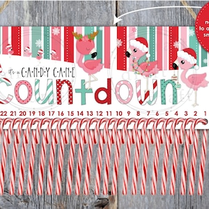 May include: A white Christmas countdown sign with pink flamingos wearing Santa hats. The sign says "It's a Candy Cane Countdown" and has 24 candy canes hanging from it.
