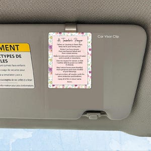 Könnte beinhalten: Ein Auto-Sonnenblenden-Clip mit rosa Hintergrund und floralem Rand. Der Clip zeigt den Text "A Traveler's Prayer" und ein Gebet. Die Worte "Car Visor Clip" sind auf der rechten Seite aufgedruckt.