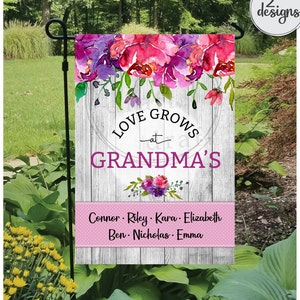 Puede incluir: Una bandera de jardín rosa y blanca con un diseño floral y el texto "Love Grows at Grandma's". Los nombres Connor, Riley, Kara, Elizabeth, Ben, Nicholas y Emma están listados debajo del texto.