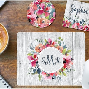 May include: A white woodgrain mousepad with a floral design and a gray circle with the initials "SMR" in the center. The floral design features pink, red, and orange flowers with green leaves.