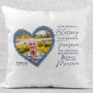 Puede incluir: Almohada blanca con un marco azul en forma de corazón que contiene una foto de un hombre. El texto dice "Your life was a Blessing Your memory a Treasure You are loved beyond words & missed beyond Measure" con el nombre "MARCUS" y las fechas "2/4/60 - 4/7/24" debajo de la foto.