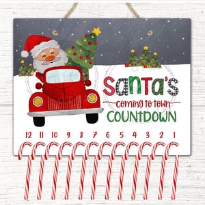 May include: A white sign with a red truck carrying a Christmas tree and Santa Claus driving. The sign says "Santa's coming to town COUNTDOWN" with 12 candy canes hanging below.