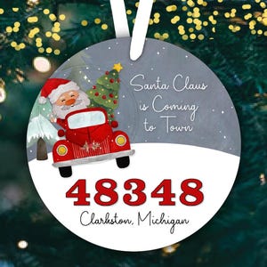 May include: A round Christmas ornament with a red truck carrying a Christmas tree. Santa Claus is coming to town text is on the ornament. The ornament also has the address 48348 Clarkston, Michigan.