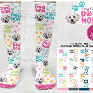 Puede incluir: Calcetines blancos con la cara de un perro y el texto "very best dog mom" en diferentes colores y patrones. Los calcetines se muestran sobre un fondo blanco con una variedad de otros diseños y combinaciones de colores.
