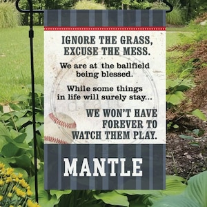 May include: A blue and white striped garden flag with a baseball theme. The flag reads "Ignore the grass, excuse the mess. We are at the ballfield being blessed. While some things in life will surely stay... We won't have forever to watch them play." The flag also features a baseball and the word "MANTLE" in large white letters.