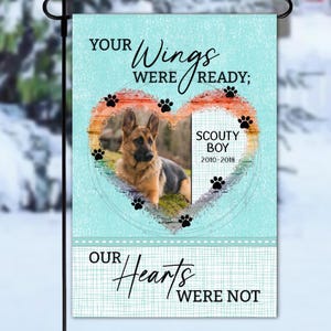May include: A garden flag featuring a German Shepherd photo within a heart design. Text reads "YOUR Wings WERE READY; OUR Hearts WERE NOT" and "SCOUTY BOY 2010-2018". The background is a light blue colour.