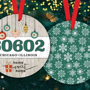 Puede incluir: Dos adornos navideños redondos. Un adorno es blanco con textura de madera y presenta el texto "60602 Chicago, Illinois" y "home sweet home" con un gráfico de caja de regalo roja. El otro adorno es verde con un patrón de copo de nieve blanco.
