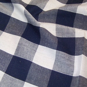May include: A white and navy blue gingham fabric with a woven texture. The fabric is folded and creased, creating a diagonal pattern.