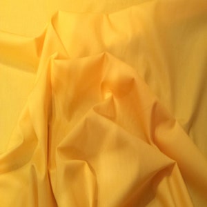 Könnte beinhalten: Nahaufnahme eines leuchtend gelben Stoffes mit weichen Falten und Schatten. Der Stoff scheint leicht zu sein, möglicherweise Baumwolle oder Leinen, mit einer glatten Textur. Die Farbe ist ein sonniges Gelb.