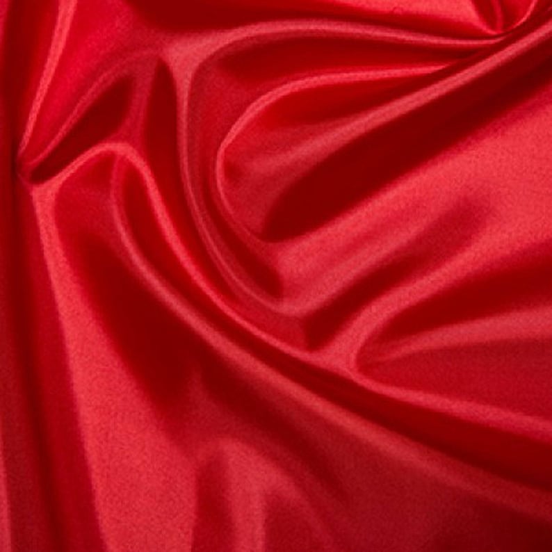 May include: Close-up of a vibrant red fabric with a silky, flowing texture. The material is draped in soft folds, creating shadows and highlights that emphasize its smooth surface. The fabric appears to be lightweight and suitable for various applications.