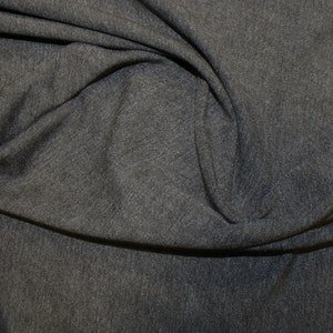Könnte beinhalten: Nahaufnahme eines dunkelgrauen Stoffes mit weicher, strukturierter Oberfläche. Der Stoff ist drapiert und gefaltet, wodurch Schatten und Lichtreflexe entstehen, die seine Textur und seinen Fall betonen. Das Material scheint ein Strick- oder Jersey-Stoff zu sein.