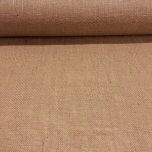 K&ouml;nnte beinhalten: Eine Rolle aus nat&uuml;rlichem braunem Jutegewebe. Der Stoff ist mit einer lockeren, offenen Webart gewebt und hat eine raue Textur.