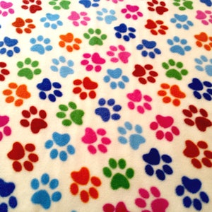 May include: White fabric with a repeating pattern of colourful paw prints. The paw prints are in shades of red, orange, yellow, green, blue, and pink.