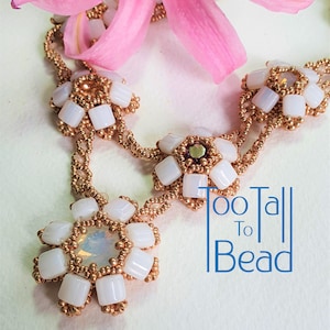 Puede incluir: Un collar de cuentas blancas con detalles dorados y un gran colgante de flor. El collar está hecho de pequeñas cuentas cuadradas y tiene un aspecto delicado y femenino. El colgante es una gran flor con un centro blanco y pétalos dorados. El collar se muestra sobre un fondo blanco con una flor rosa.