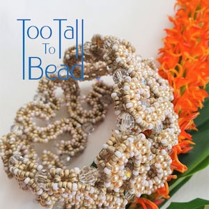 May include: A beige and white beaded bracelet with a delicate, intricate design. The bracelet is made with small, round beads and features a subtle shimmer.