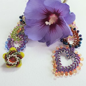 May include: A purple flower with a beaded necklace featuring a yellow flower charm and two heart-shaped charms with purple and orange beads.