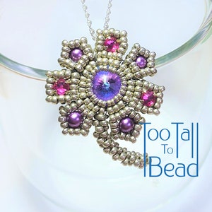 May include: A silver beaded flower pendant with purple and pink beads and a large purple crystal in the centre. The pendant is hanging from a silver chain. The text "Too Tall To Bead" is visible in the bottom right corner of the image.
