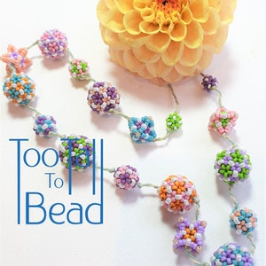 May include: A colorful beaded necklace with a variety of shapes and sizes. The beads are made of small seed beads and are strung on a thin thread. The necklace is displayed on a white background with a yellow flower.