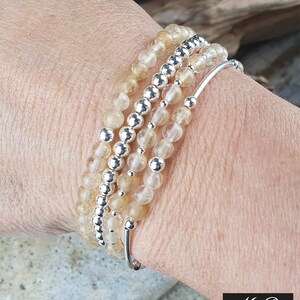 May include: A set of four bracelets featuring clear quartz beads with a subtle golden hue and silver spacer beads. The bracelets are stacked on a person's wrist.