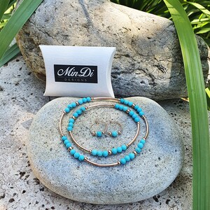 Può includere: Un set di gioielli in turchese e oro con un paio di orecchini a cerchio e due collane. I gioielli sono esposti su una roccia grigia con una scatola a cuscino bianca che dice "Min Di Designs".