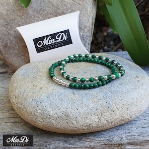 May include: Two green malachite and silver bead bracelets stacked on a grey stone. The bracelets are packaged in a white box with the text "Min Di Designs" printed on it.