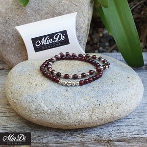 May include: Two garnet gemstone bracelets with silver beads. The bracelets are stacked on top of each other and are on a grey rock. The bracelets are packaged in a white pillow box with the text "Min Di Designs" printed on the box.