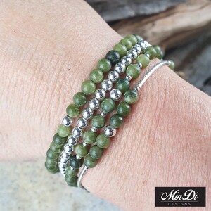 May include: A set of four green jade stone bracelets with silver beads. The bracelets are stacked on a person's wrist.