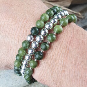 May include: A set of three green and silver beaded bracelets. The bracelets are made with green jade-like stones and silver beads. The bracelets are stacked on a person's wrist.