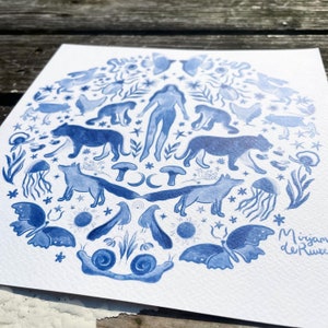 May include: A blue and white watercolor illustration of a circle with various animals, plants, and celestial objects. The illustration includes a woman, foxes, butterflies, mushrooms, snails, stars, and a crescent moon. The artist's name, "Mirjam de Ruwe", is written in the bottom right corner.