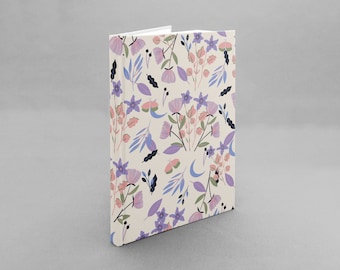 Puede incluir: Un cuaderno de color crema con un patrón floral con flores rosas, moradas y azules, hojas y lunas crecientes.