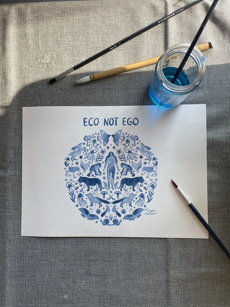 May include: A blue and white watercolor illustration of a circle with a woman in the center surrounded by animals, plants, and other natural elements. The text "ECO NOT EGO" is at the top of the circle. The artist's signature is at the bottom of the circle.