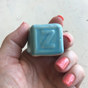 Puede incluir: Un bloque de cerámica azul claro con la letra "Z" en relieve.