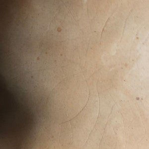 May include: Close-up of a light brown ceramic surface with a subtle pattern of lines and a few brown spots.