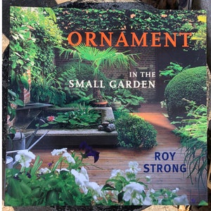May include: A book titled "Ornament in the Small Garden" by Roy Strong. The cover features a lush, green garden with a small pond, a wooden deck, and a variety of plants.