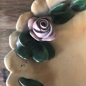 May include: A cream-colored ceramic dish with a scalloped edge. The dish is decorated with a pink rose and green leaves.