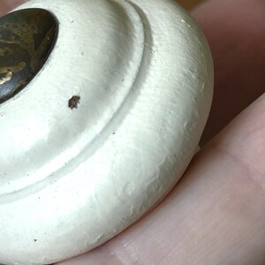 Peut inclure: Gros plan sur un bouton de tiroir blanc de style antique avec une surface textur&eacute;e. Le bouton a une forme arrondie avec un accent en m&eacute;tal de couleur laiton. Le design pr&eacute;sente un motif tourbillonnant.