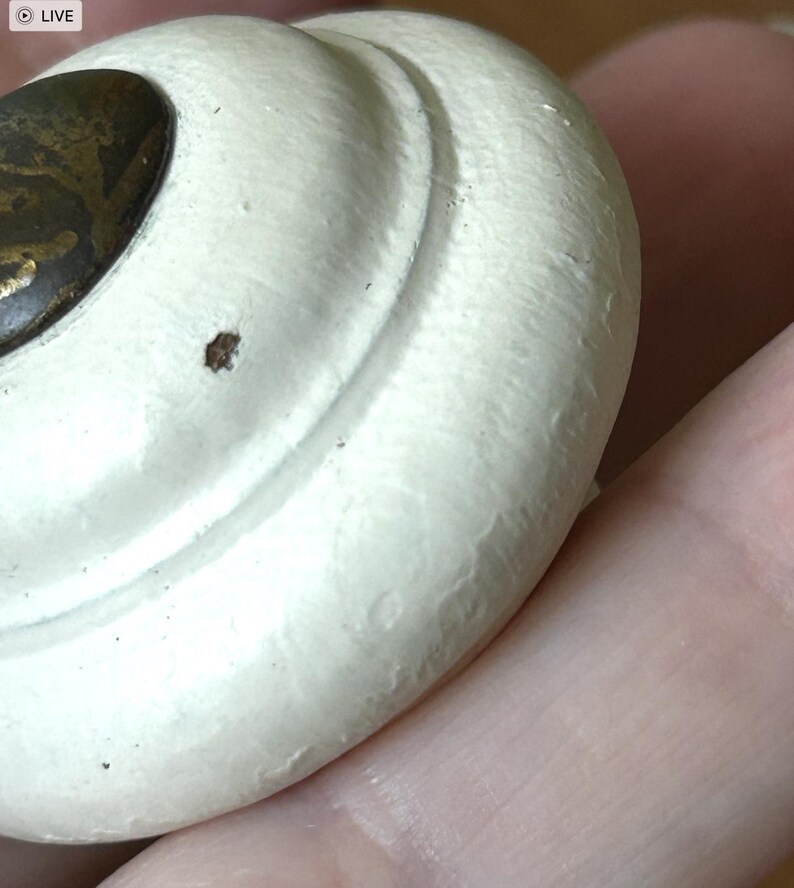 Peut inclure: Gros plan sur un bouton de tiroir blanc de style antique avec une surface textur&eacute;e. Le bouton a une forme arrondie avec un accent en m&eacute;tal de couleur laiton. Le design pr&eacute;sente un motif tourbillonnant.
