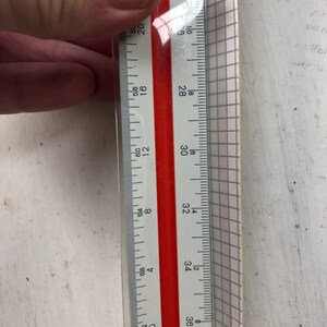 Puede incluir: Una regla blanca con marcas rojas, que muestra medidas en pulgadas y fracciones de pulgada. La regla está marcada de 20 a 36 pulgadas.