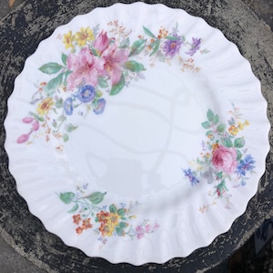 Puede incluir: Plato de cena de cerámica blanca con borde festoneado y diseño floral con flores rosas, amarillas y azules.