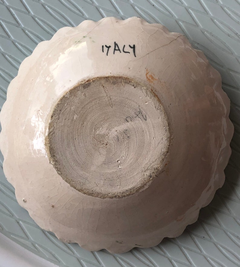 May include: White ceramic bowl with a scalloped edge and a brown glaze on the inside. The bottom of the bowl has the number "17 ACY" written in black.